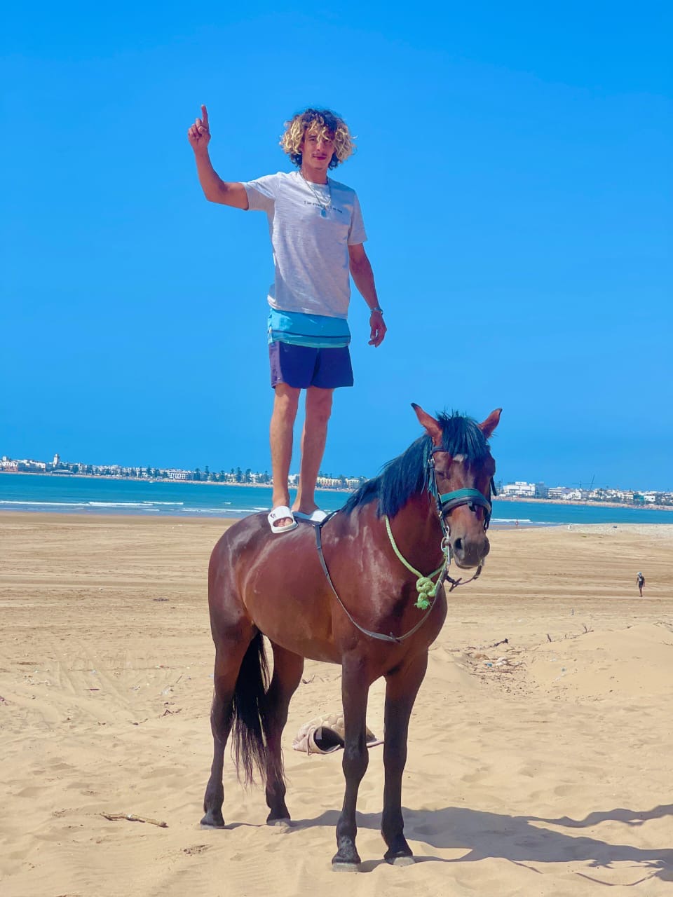 Mokhtar debout sur le dos d'Assif, Essaouira en arrière-plan
